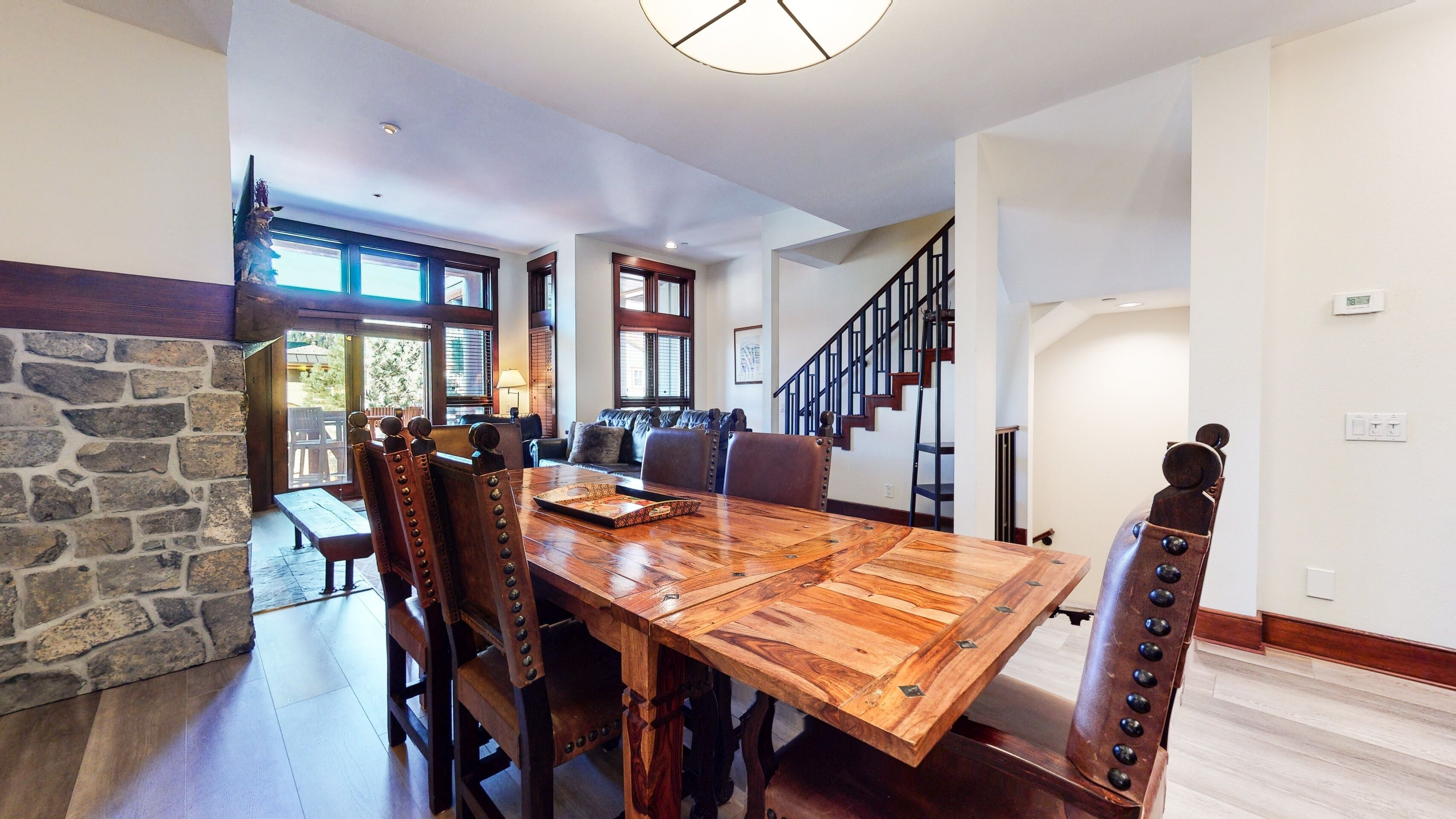 Un vaste espace dédié à la salle à manger, avec une grande table et des chaises en bois, un mur décoratif en pierre et un escalier menant à un niveau supérieur.