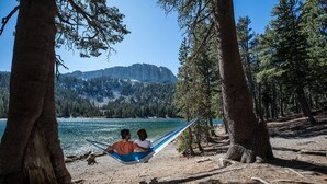 Un hamac tendu entre deux arbres, d’où l’on a une vue sur un lac, avec des montagnes en arrière-plan.