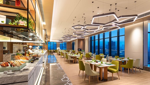 A modern dining area with a long counter, multiple tables, and chairs. - Holiday Inn Hangzhou Binjiang (Hangzhou)