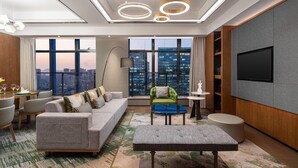 A modern living room with a sofa, ottoman, and a green armchair. A flat-screen TV is mounted on the wall, and there is a city view through large windows. - Holiday Inn Hangzhou Binjiang (Hangzhou)
