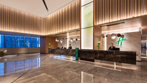 A modern hotel lobby with a reception desk, large windows, and a wooden panel wall. - Holiday Inn Hangzhou Binjiang (Hangzhou)
