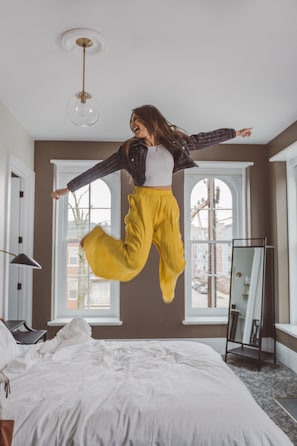 Quarto com cama, abajur, espelho e janela com vista para edifícios.