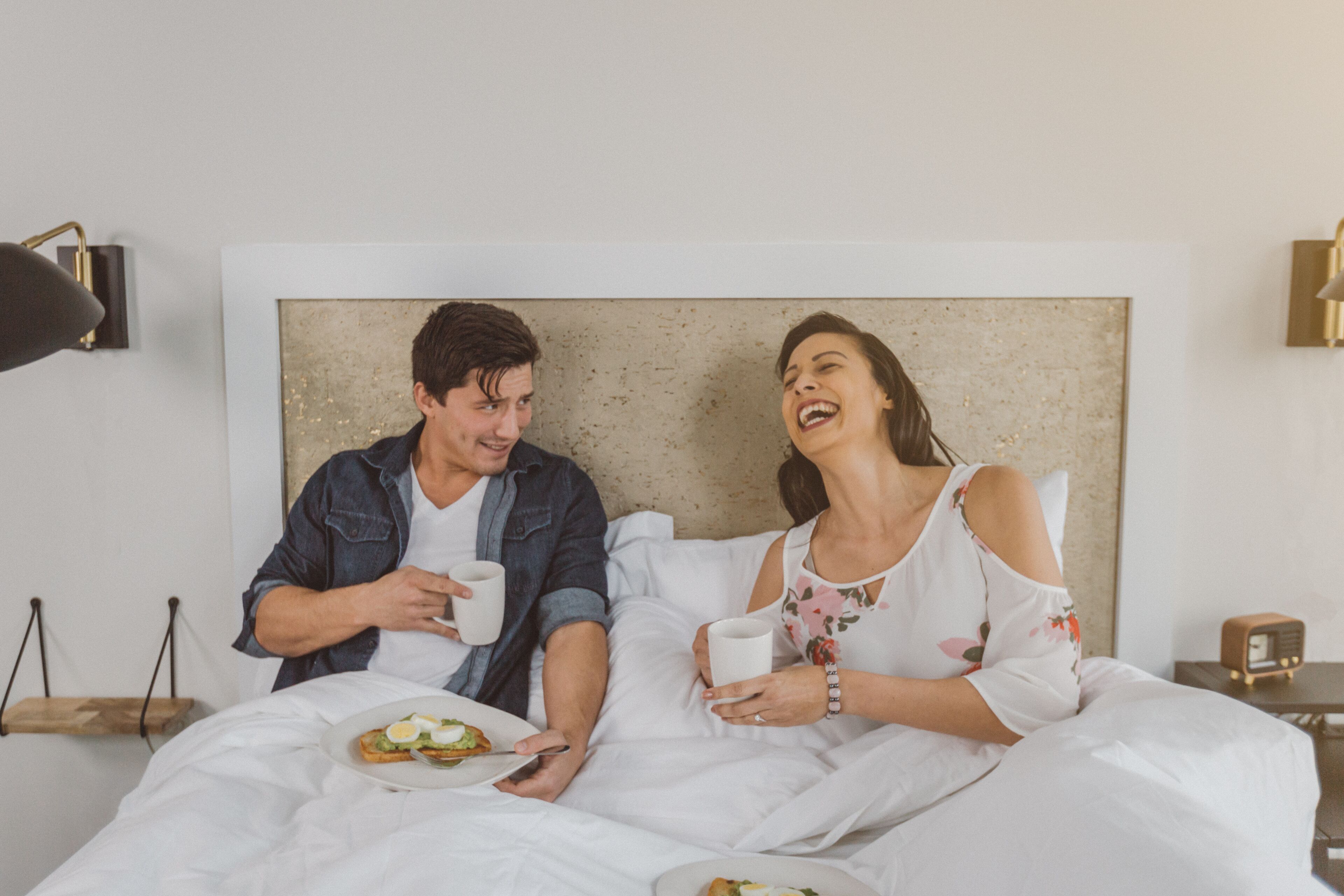 Una pareja en la cama con platos de desayuno y tazas de café.