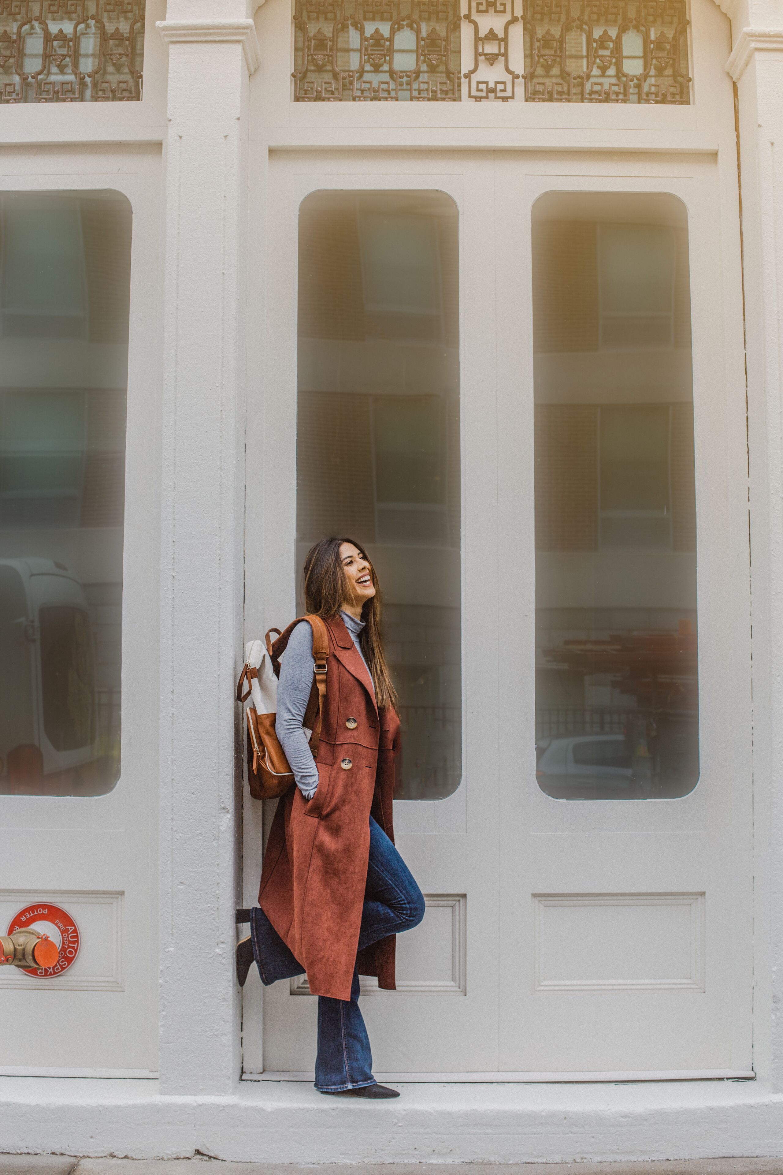 A person leaning against a white building with large windows and a door.