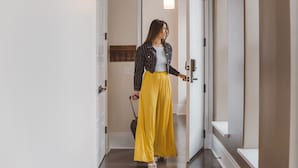 A woman in a striped jacket and yellow skirt walking through a hallway with a door and a light fixture. - Hancock House (Louisville)
