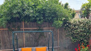 Um jardim com balanço, um sofá estampado com almofadas laranja e plantas em vasos.