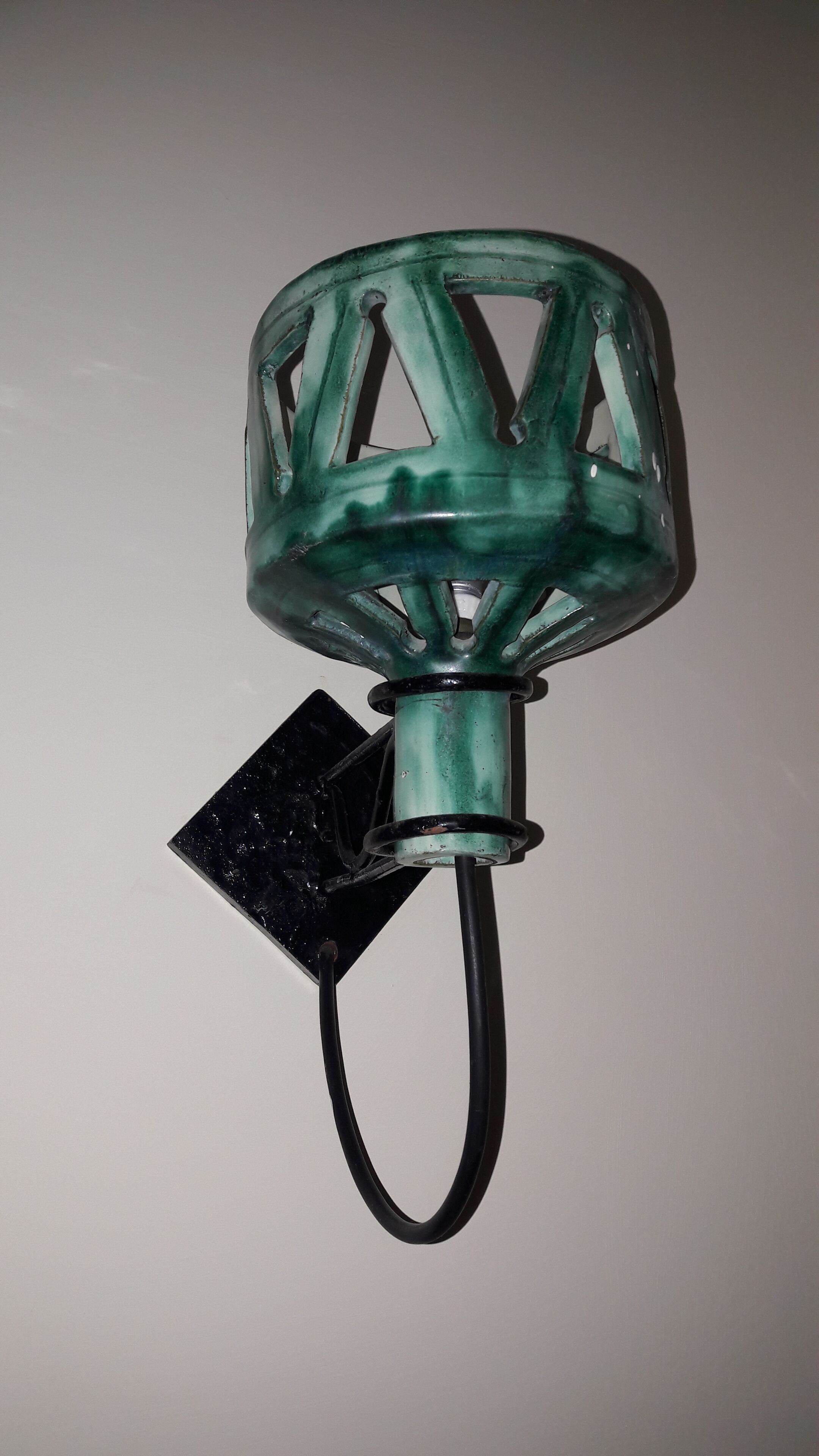 Un luminaire de couleur verte et métallique, de forme géométrique, doté d’un socle noir et d’un cordon flexible.