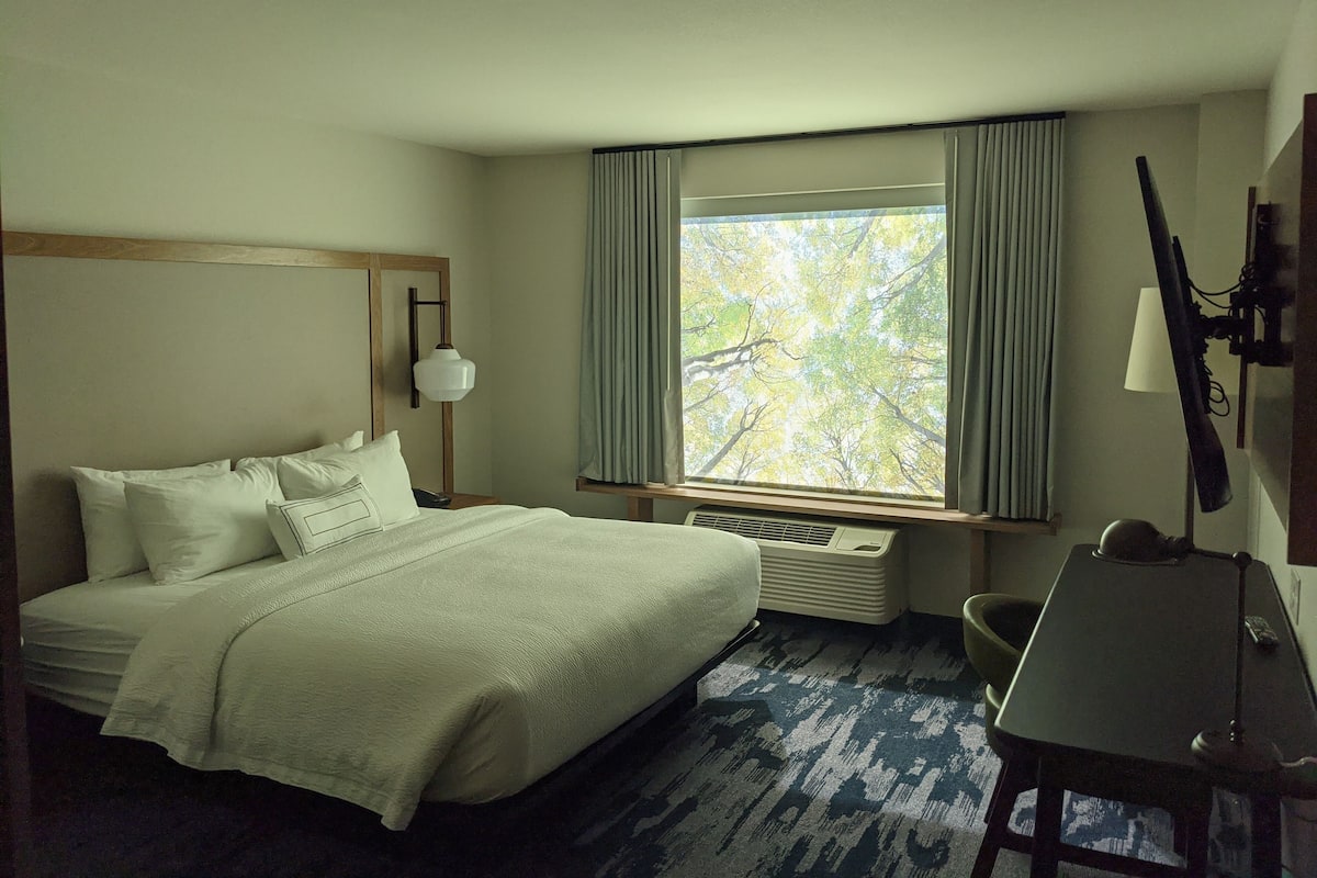 A hotel room with a bed, a desk, a chair, a window with curtains, and a mounted television.