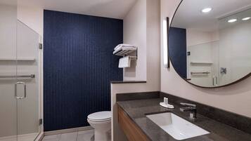 Een moderne badkamer met een glazen douchecabine, een wit toilet, een donkerblauwe wand, een witte wastafel met een marmeren aanrechtblad en een grote spiegel.