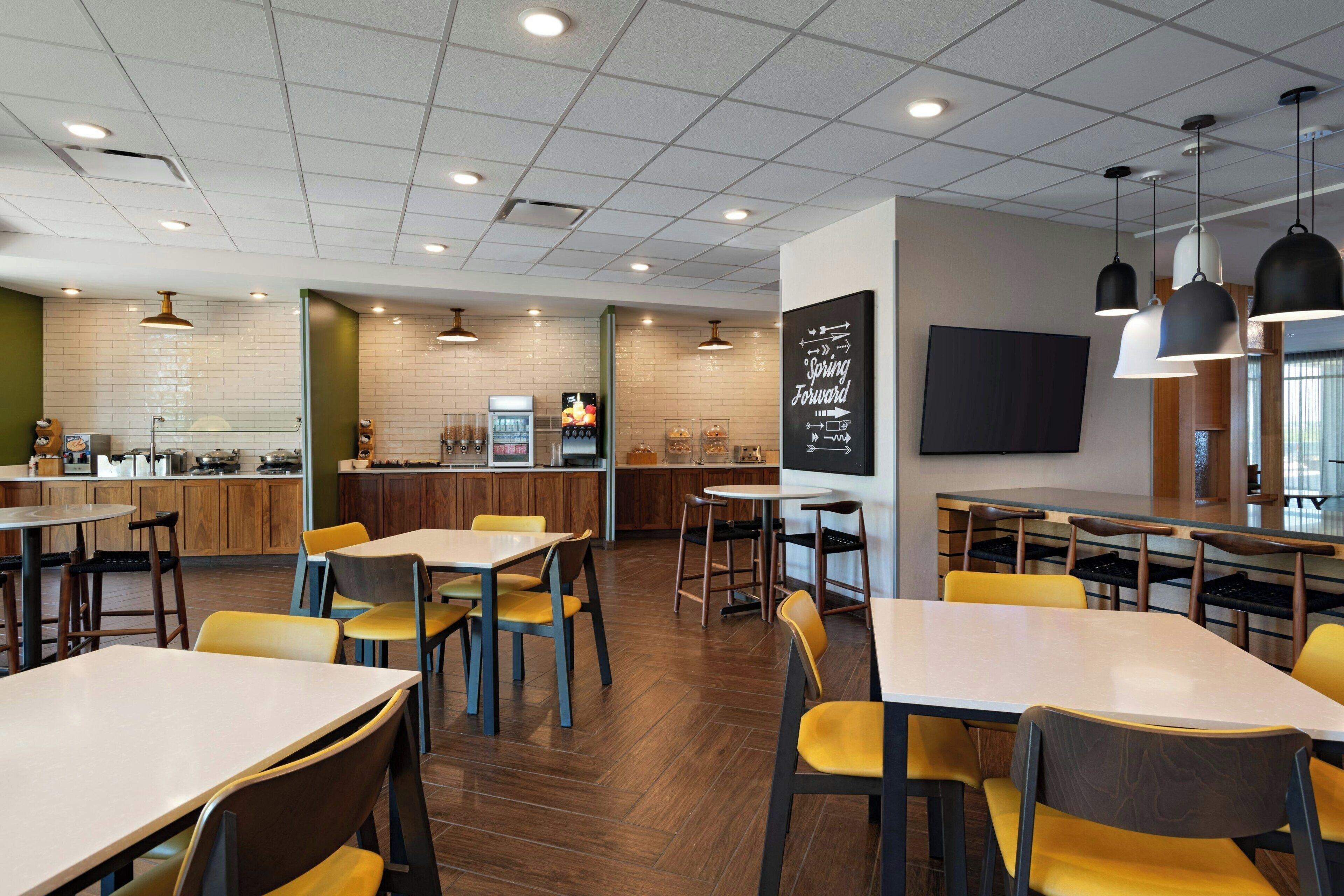 A modern restaurant with wooden flooring, yellow chairs, and a variety of seating arrangements.