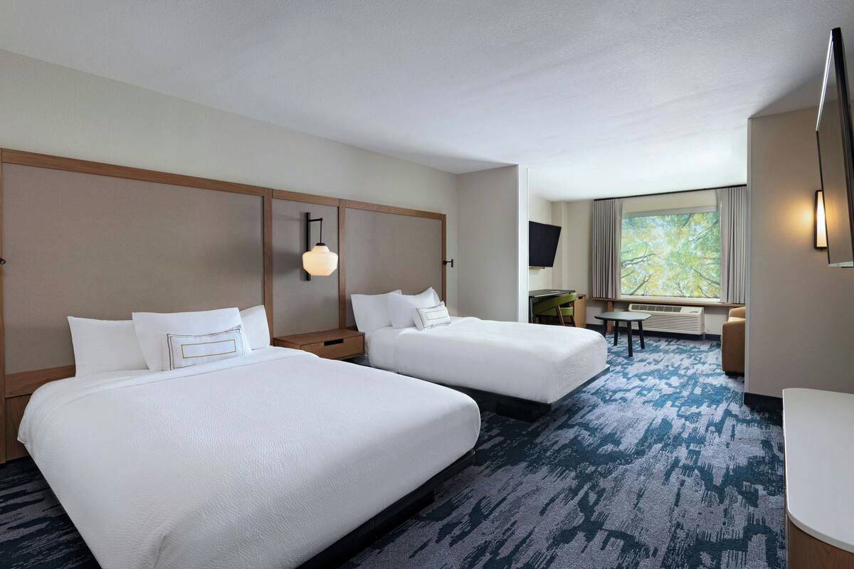 A hotel room with two beds, a desk, a chair, and a large window with curtains.