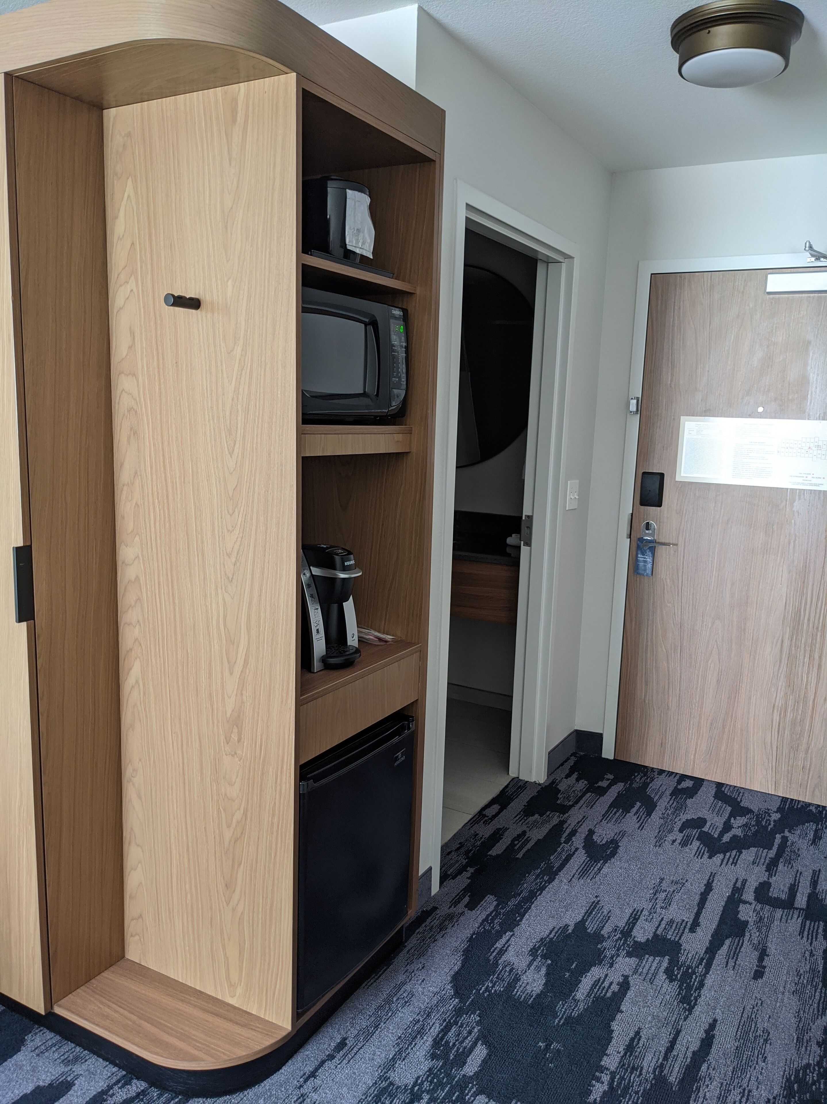 A compact room with a built-in wooden wardrobe, a microwave, a coffee maker, and a small refrigerator.