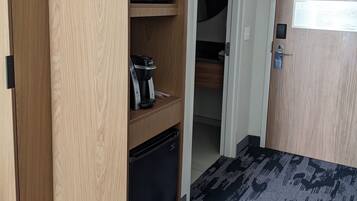 A compact room with a built-in wooden wardrobe, a microwave, a coffee maker, and a small refrigerator.