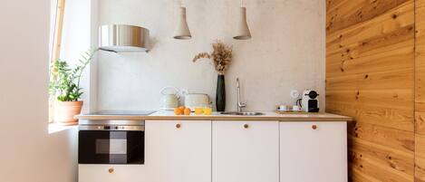 A modern kitchen with white cabinets, a stainless steel range hood, a built-in oven, a sink, and a wooden wall.