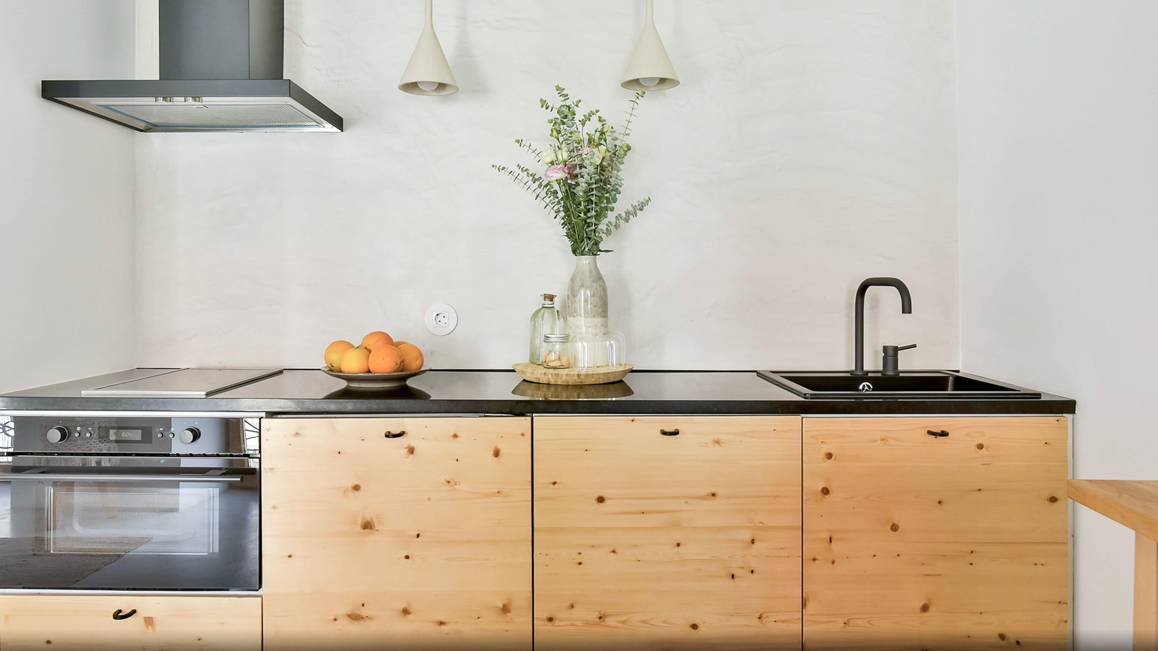 Eine moderne Küche mit schwarzem Arbeitsplatz, Holzschränken, einem eingebauten Backofen, einer Spüle und einer Vase mit Blumen.