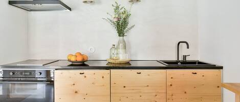 Eine moderne Küche mit schwarzem Arbeitsplatz, Holzschränken, einem eingebauten Backofen, einer Spüle und einer Vase mit Blumen.