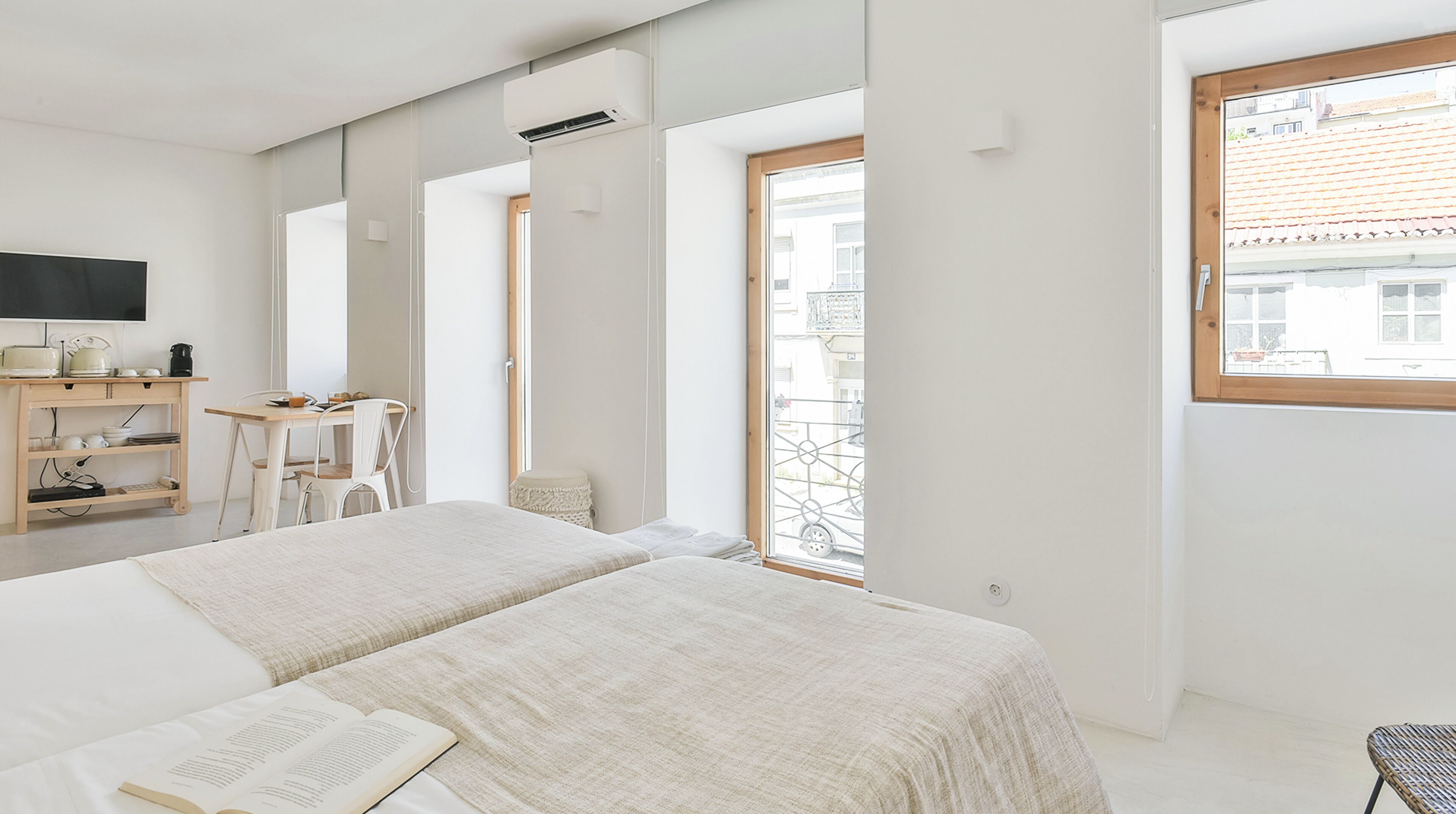 A minimalist hotel room with a large bed, a desk with a chair, a small table, and a TV.
