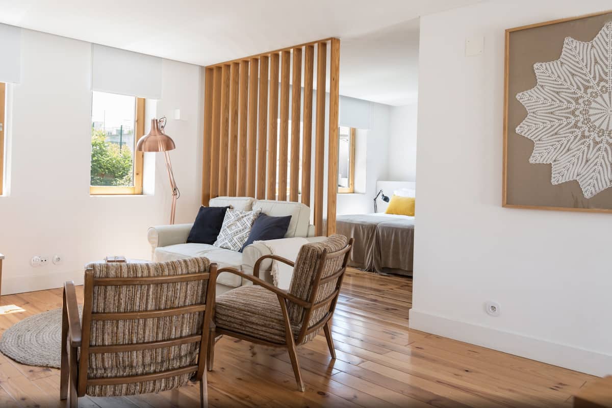 Un salon moderne avec un plancher en bois, un canapé, deux fauteuils, une table basse et une grande fenêtre.