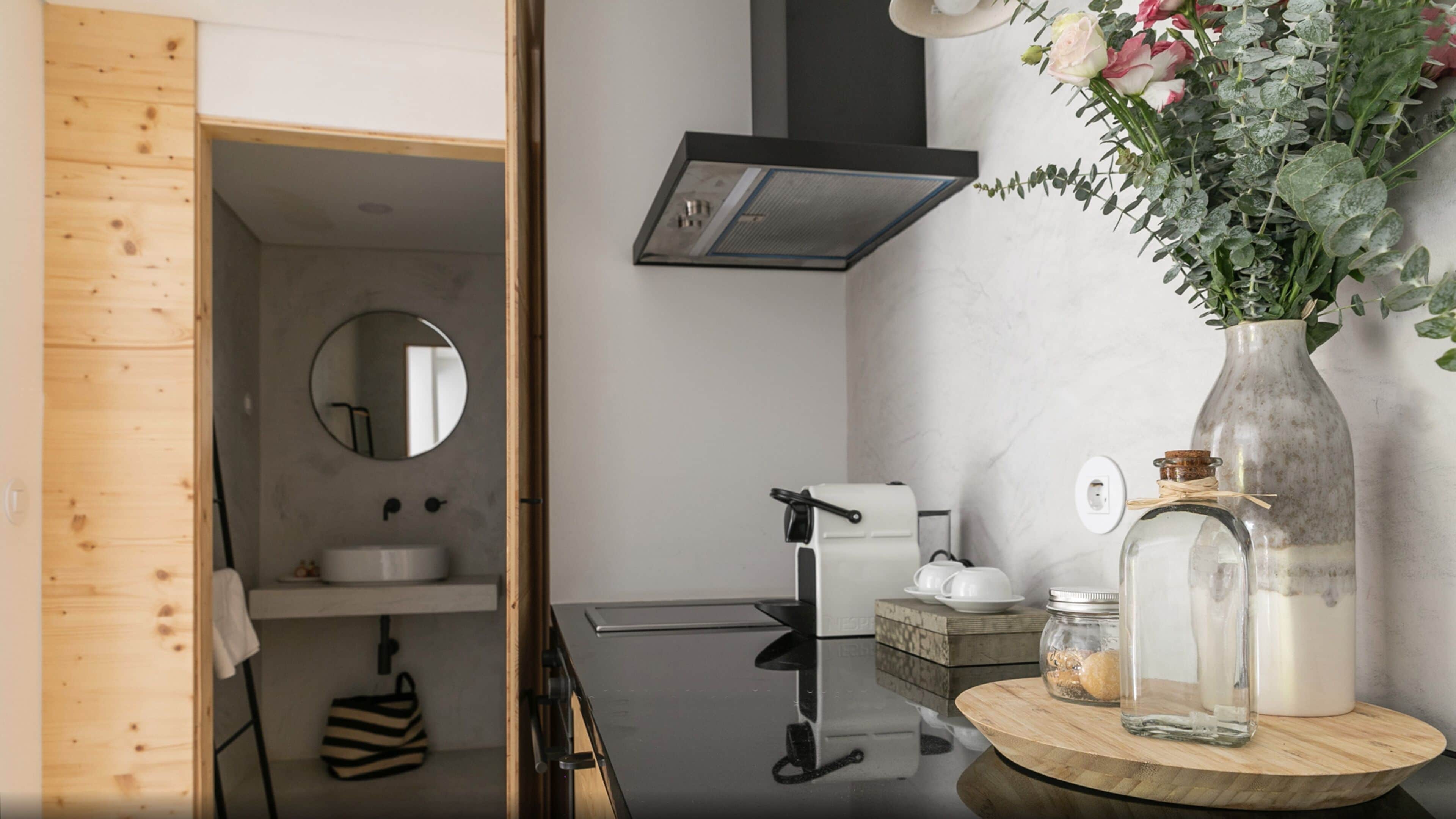 Une salle de bain moderne avec un meuble-lavabo en bois, un miroir rond, un robinet noir et un vase rempli de fleurs posé sur le plan de toilette.