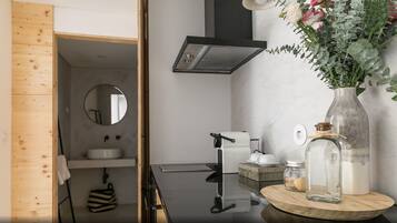 Une salle de bain moderne avec un meuble-lavabo en bois, un miroir rond, un robinet noir et un vase rempli de fleurs posé sur le plan de toilette.