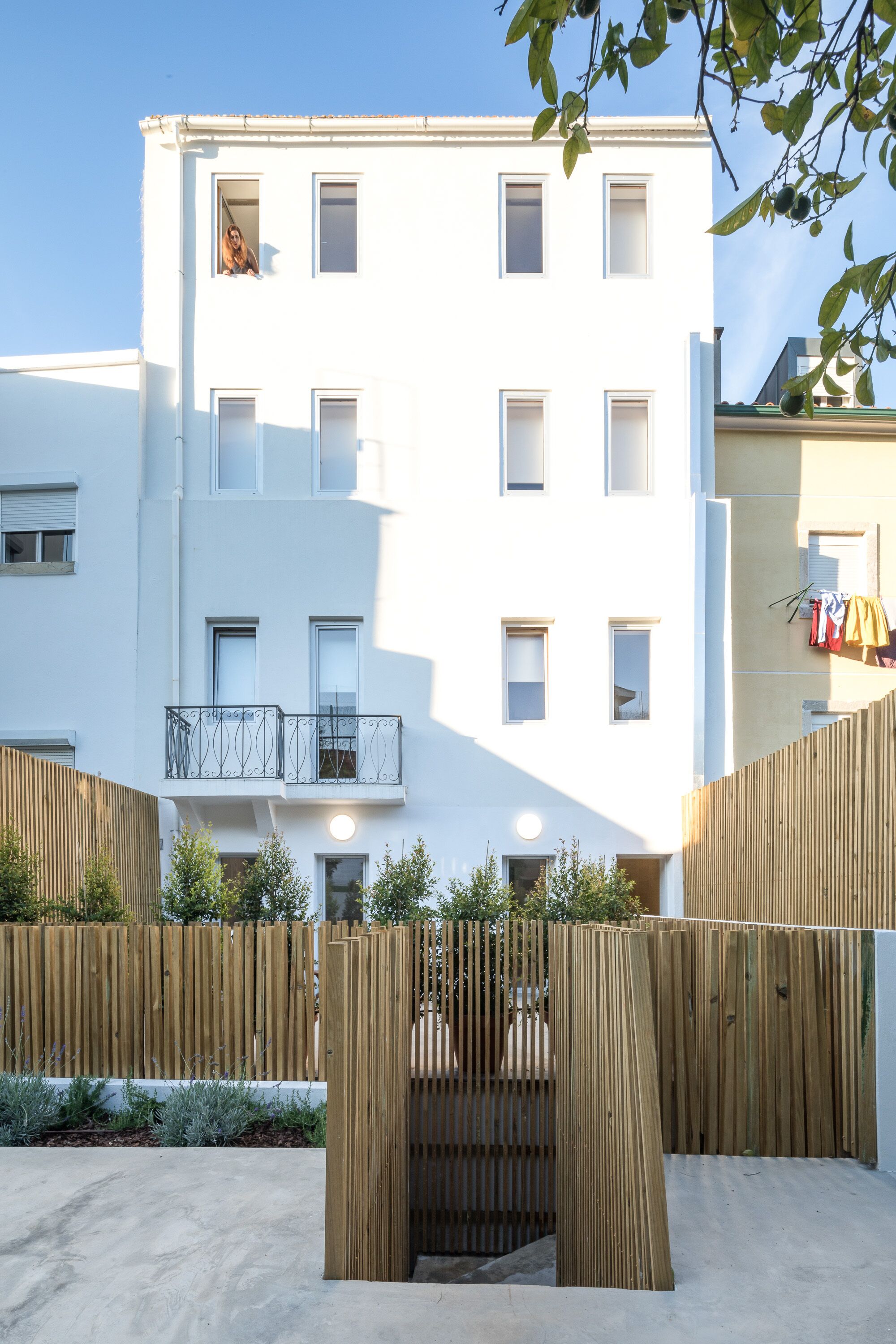 A multi-story building with a white facade, balconies, and a wooden fence in the foreground.