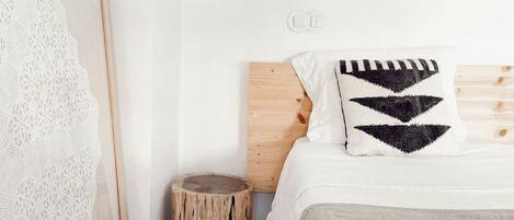A bedroom with a wooden headboard, a white bedspread, and a patterned pillow.