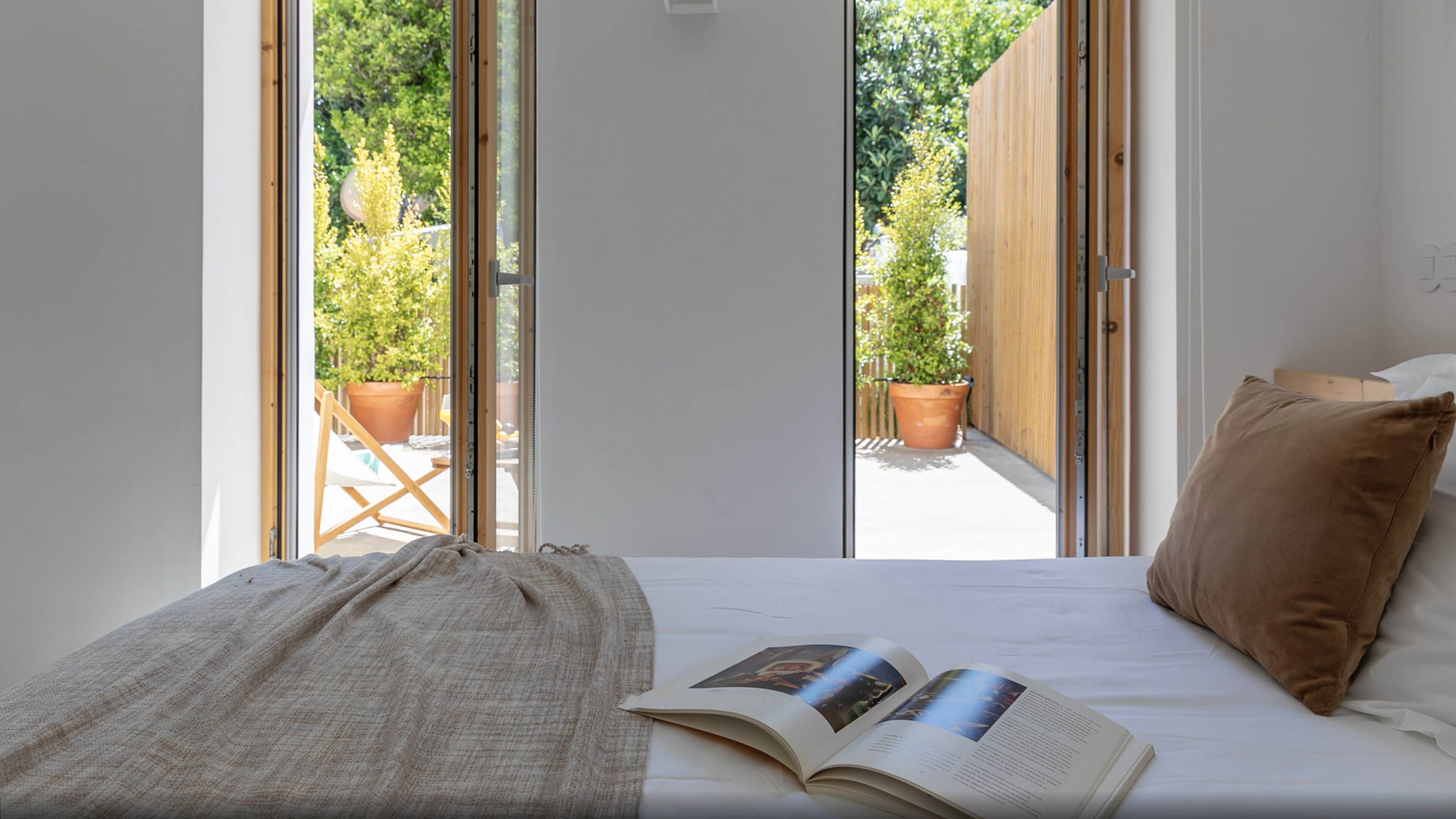 A bedroom with a bed, a book, and a view of a garden through open sliding doors.