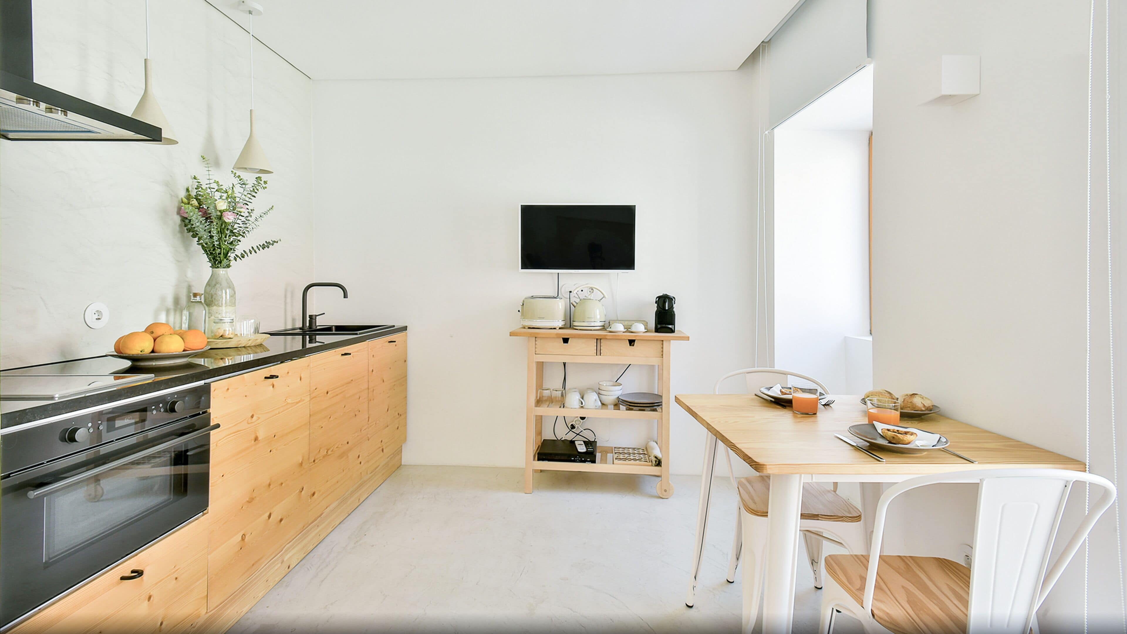 Eine moderne Küche mit Holzschränken, einem schwarzen Herd und einem Essbereich mit einem Holztisch und weißen Stühlen.