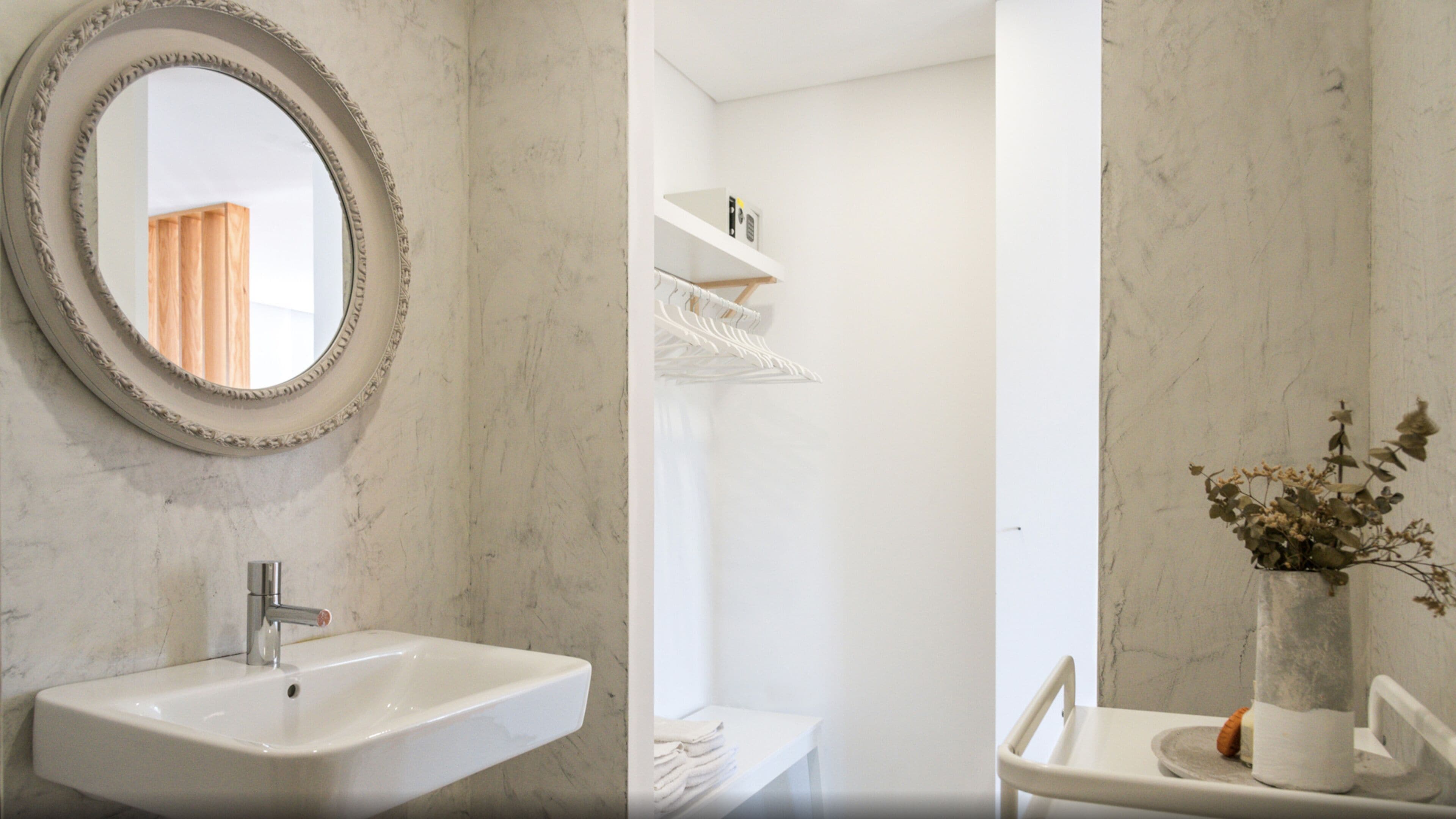 A bathroom with a marble sink, a round mirror, and a vase with dried flowers.