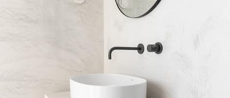 A bathroom with a white marble sink, a black faucet, and a round mirror.