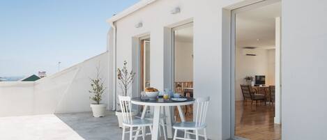 A modern outdoor dining area with a round table and white chairs, a potted plant, and a breakfast setting.