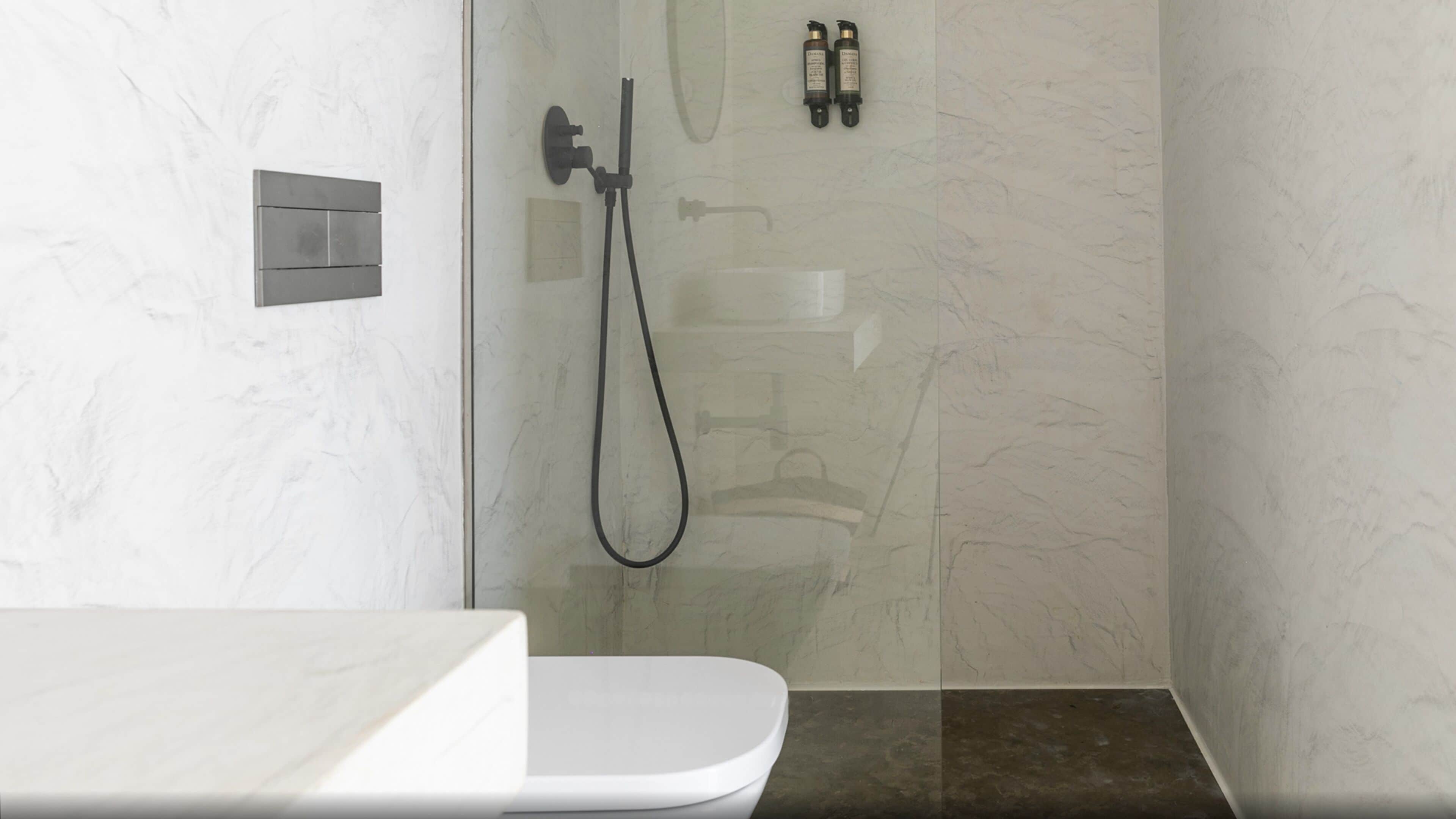 A modern bathroom with a glass shower enclosure, a white toilet, and a marble-tiled wall.
