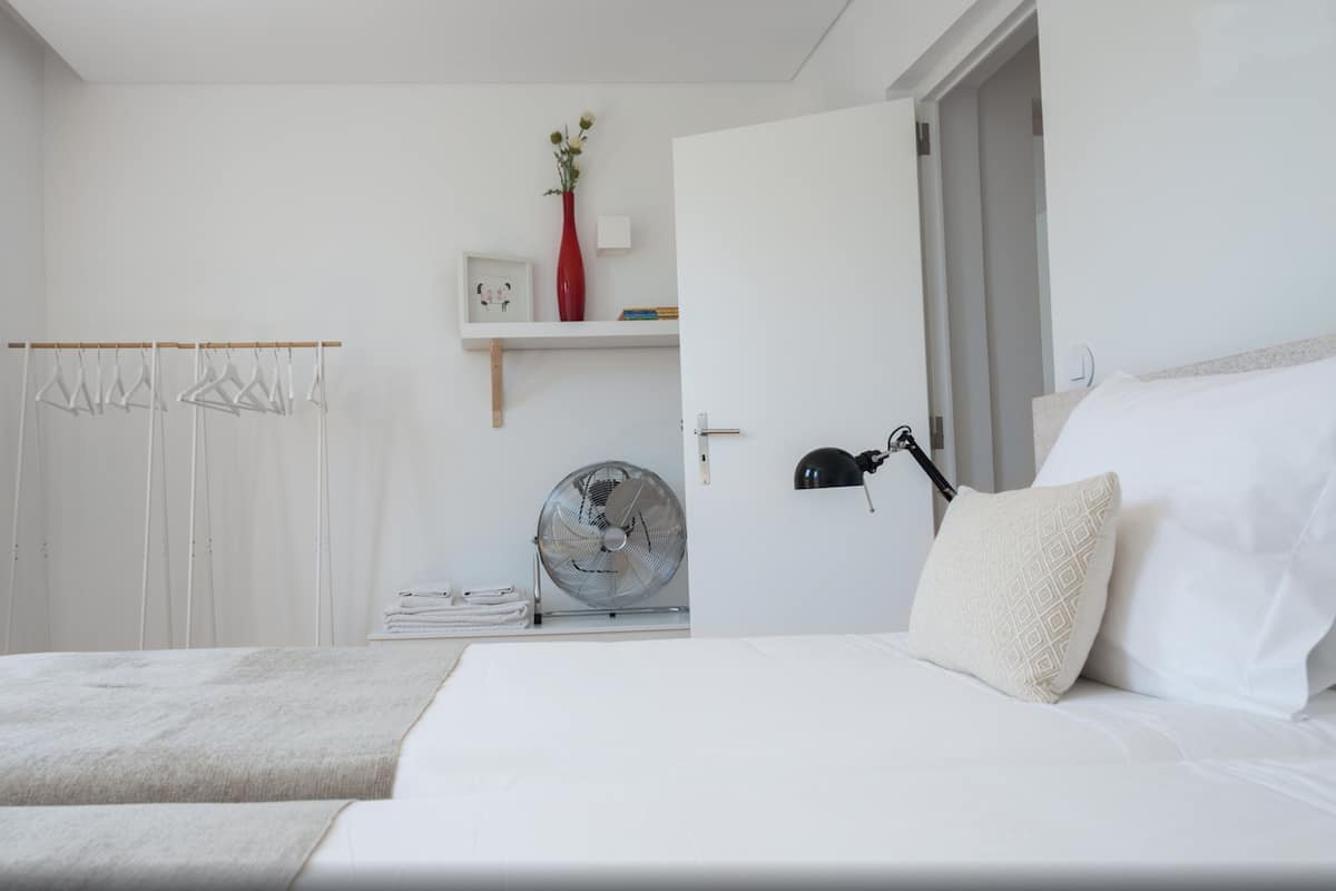 Une chambre avec deux lits, une armoire, un ventilateur, une lampe et un vase de fleurs.