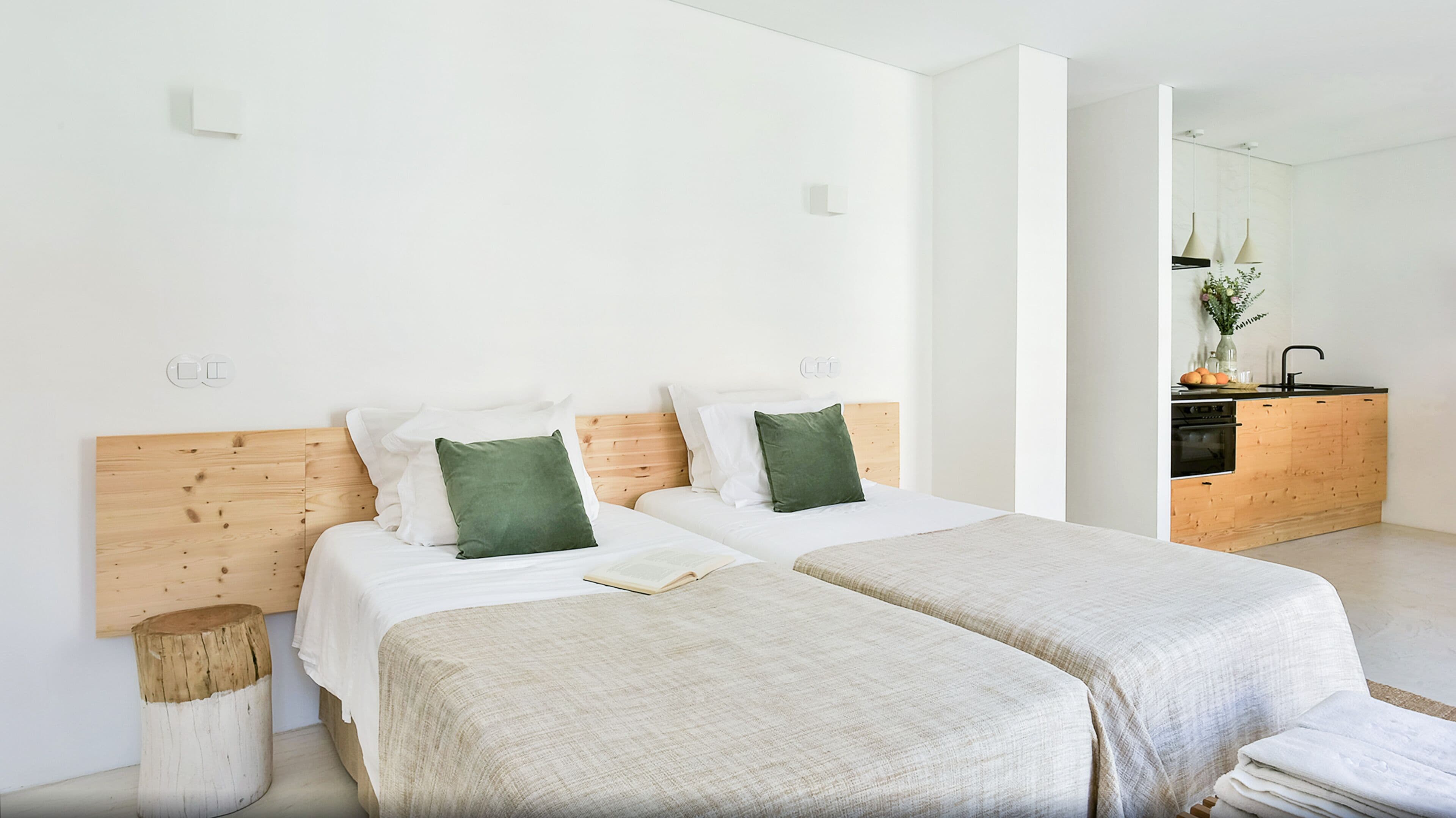 A modern bedroom with two beds, a wooden headboard, and a small bedside table.