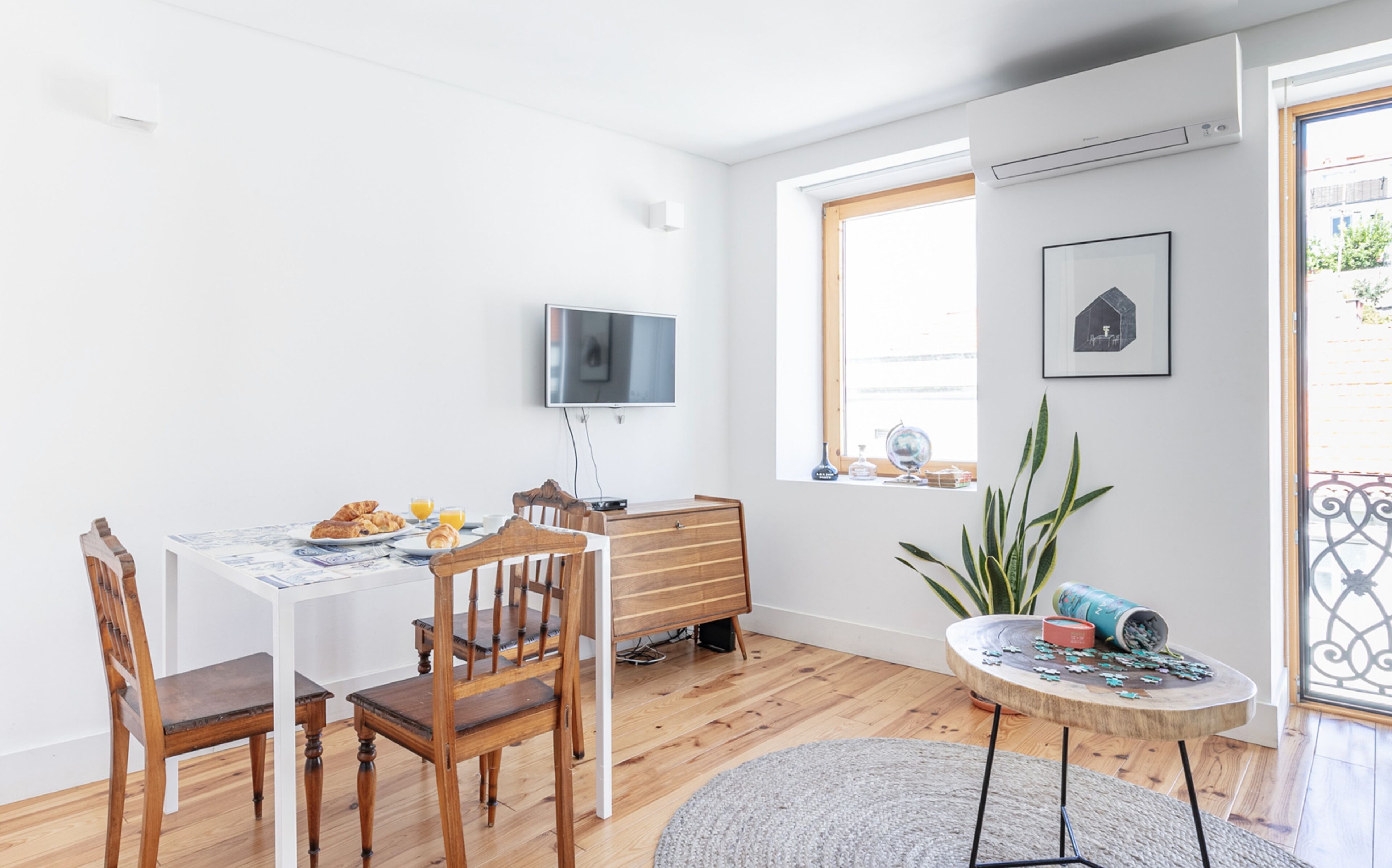 Een lichte eetruimte met een houten tafel gedekt voor het ontbijt, een aan de muur bevestigde televisie en een raam met uitzicht.