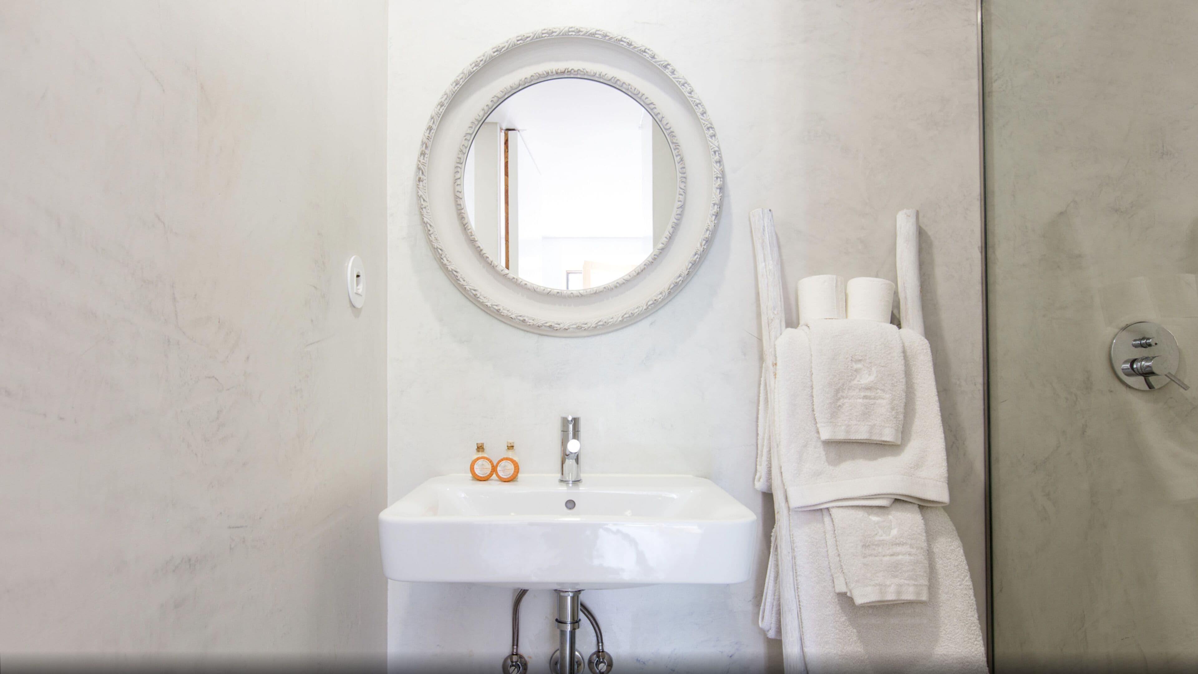 Een badkamer met een witte wastafel, een ronde spiegel en twee handdoeken aan de muur.