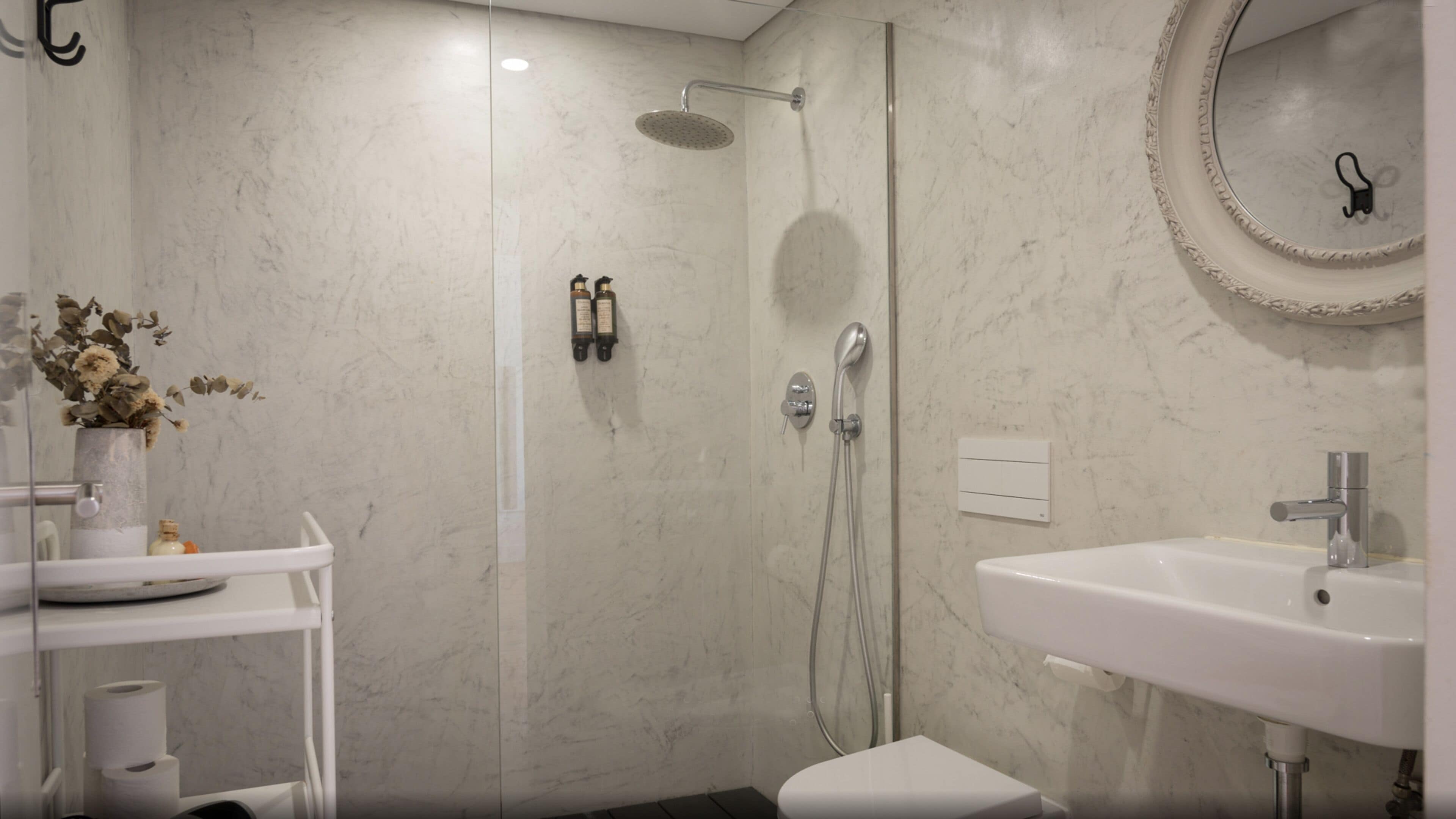 Ein modernes Badezimmer mit Dusche, Waschbecken und Toilette. Links steht eine Vase mit Blumen, rechts ein Spiegel.