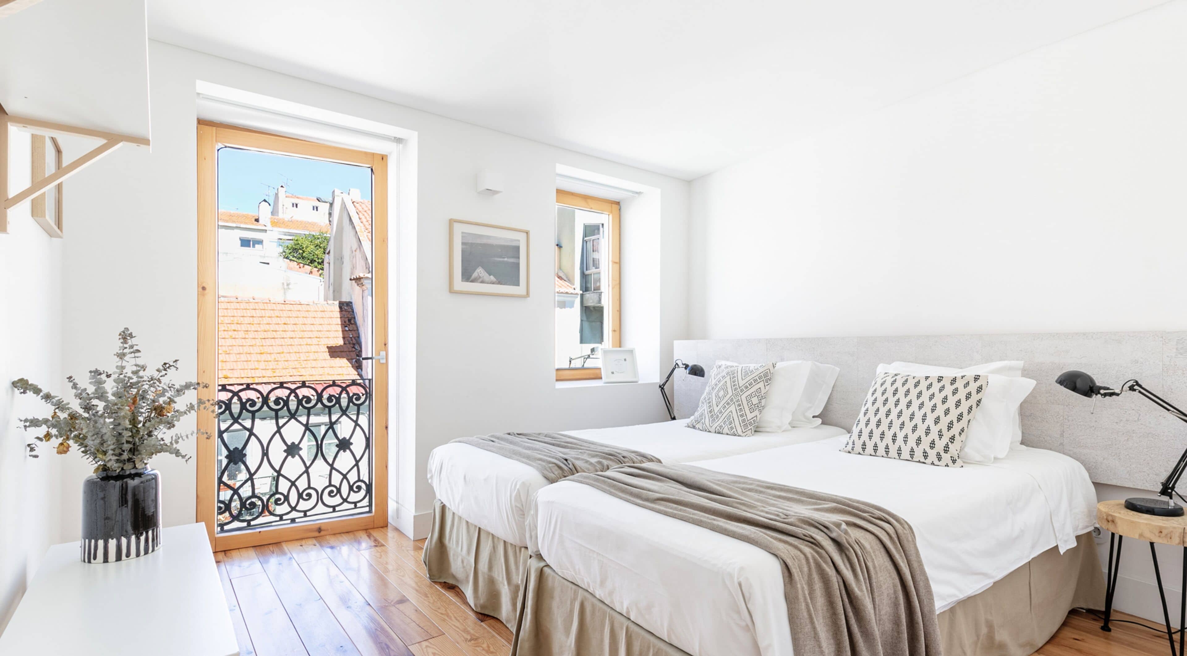 A bedroom with a bed, bedside table, lamp, and a view of the outside.