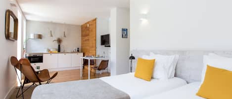 Une chambre d’hôtel moderne avec un grand lit, un petit bureau et, au fond, une kitchenette.