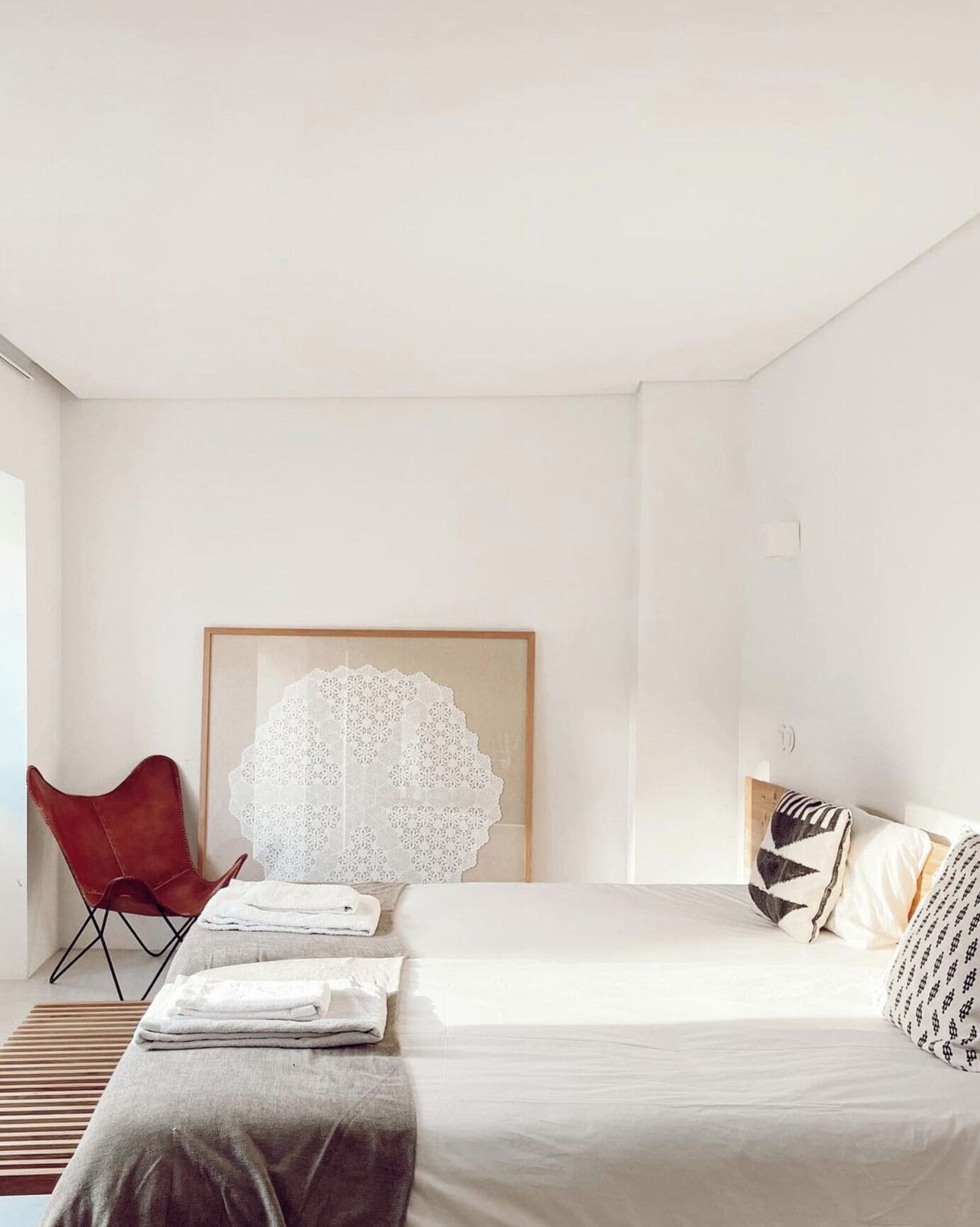 A minimalist bedroom with a bed, a red chair, and a large white artwork on the wall.