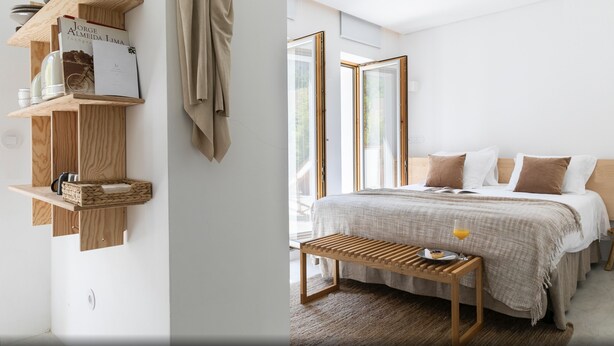 A bedroom with a bed, bedside table, and a wooden shelf with books and a lamp.