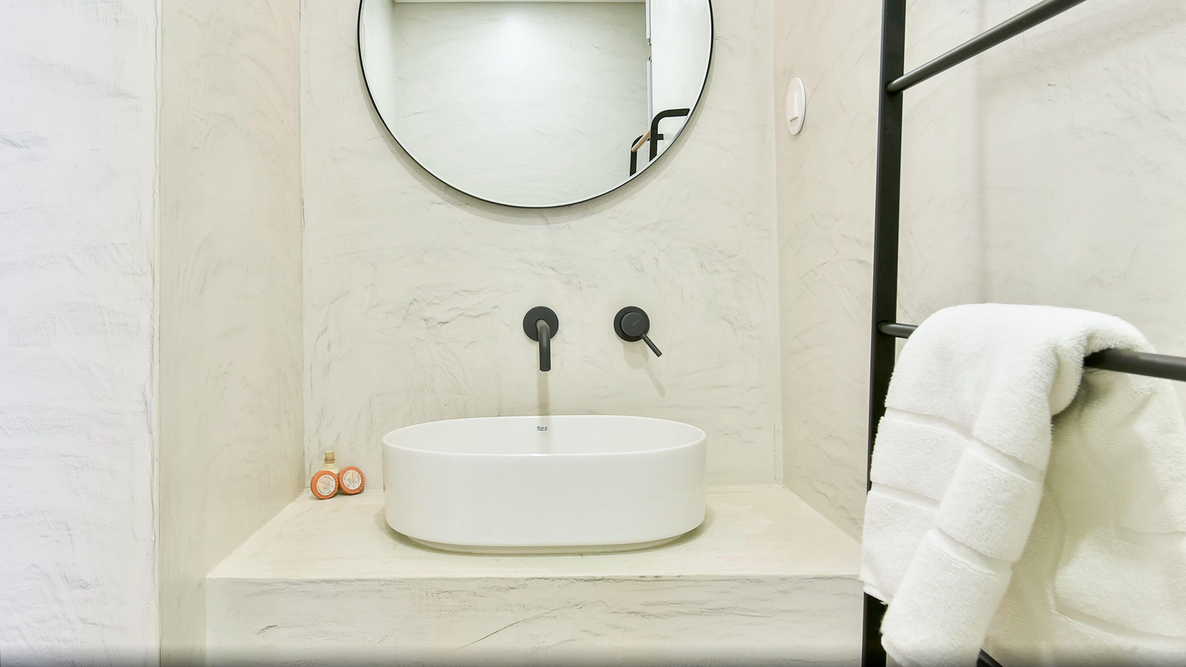 A bathroom with a white sink, a round mirror, and a towel rack.