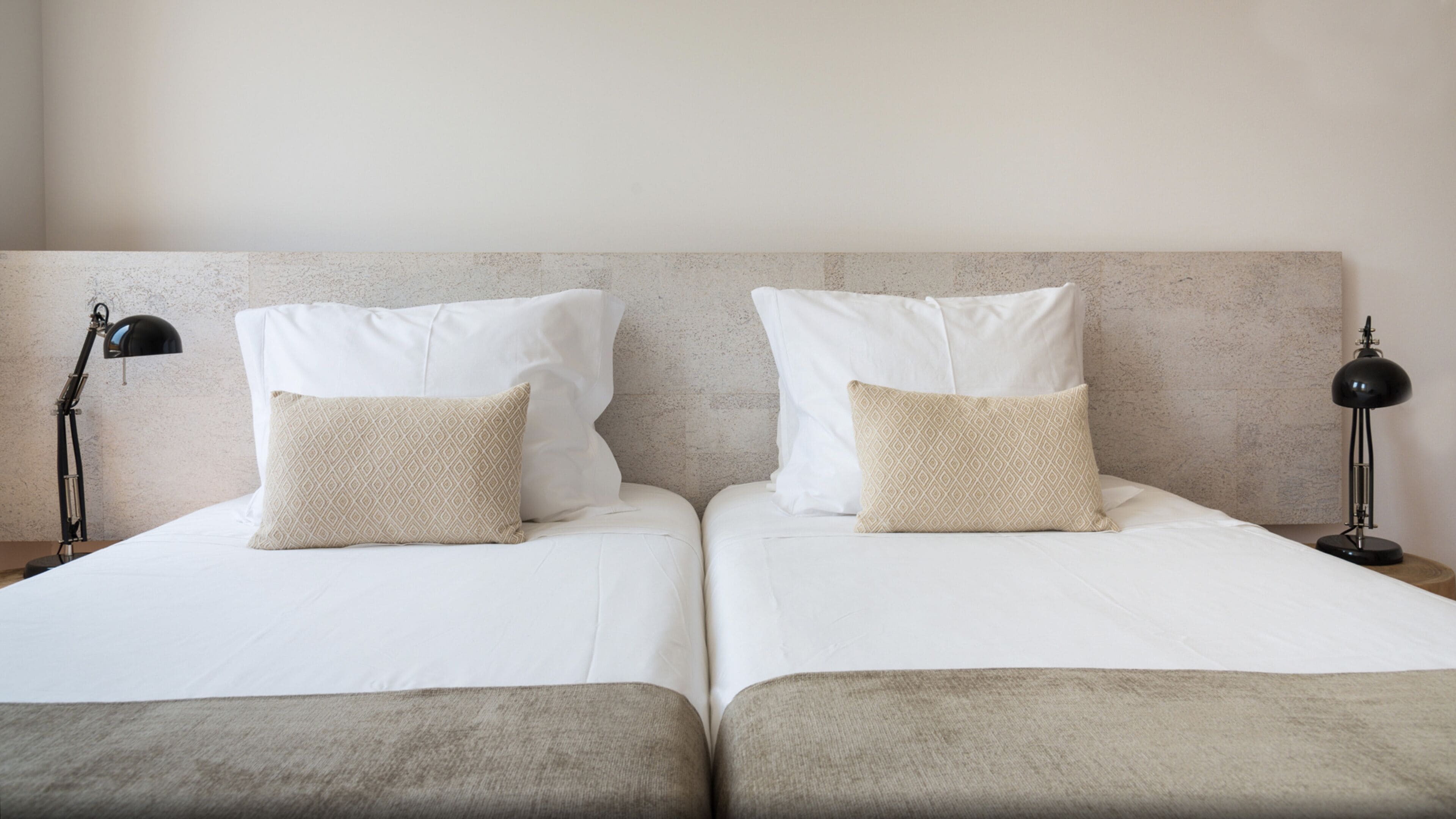 A double bed with white linens and two pillows, a bedside lamp on each side, and a textured headboard.