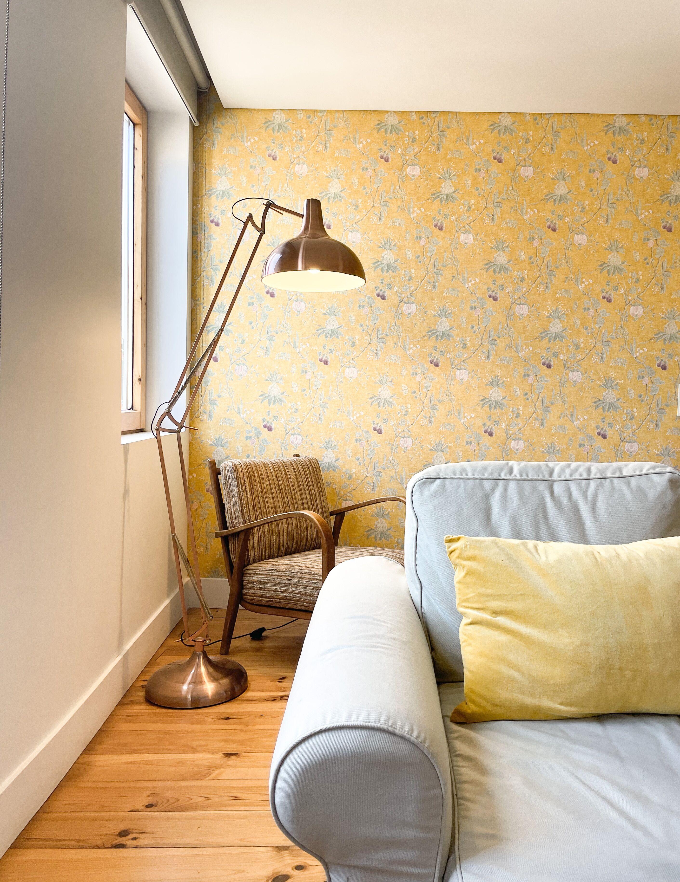 A cozy room with a wooden floor, a sofa with a cushion, a striped chair, and a floor lamp.