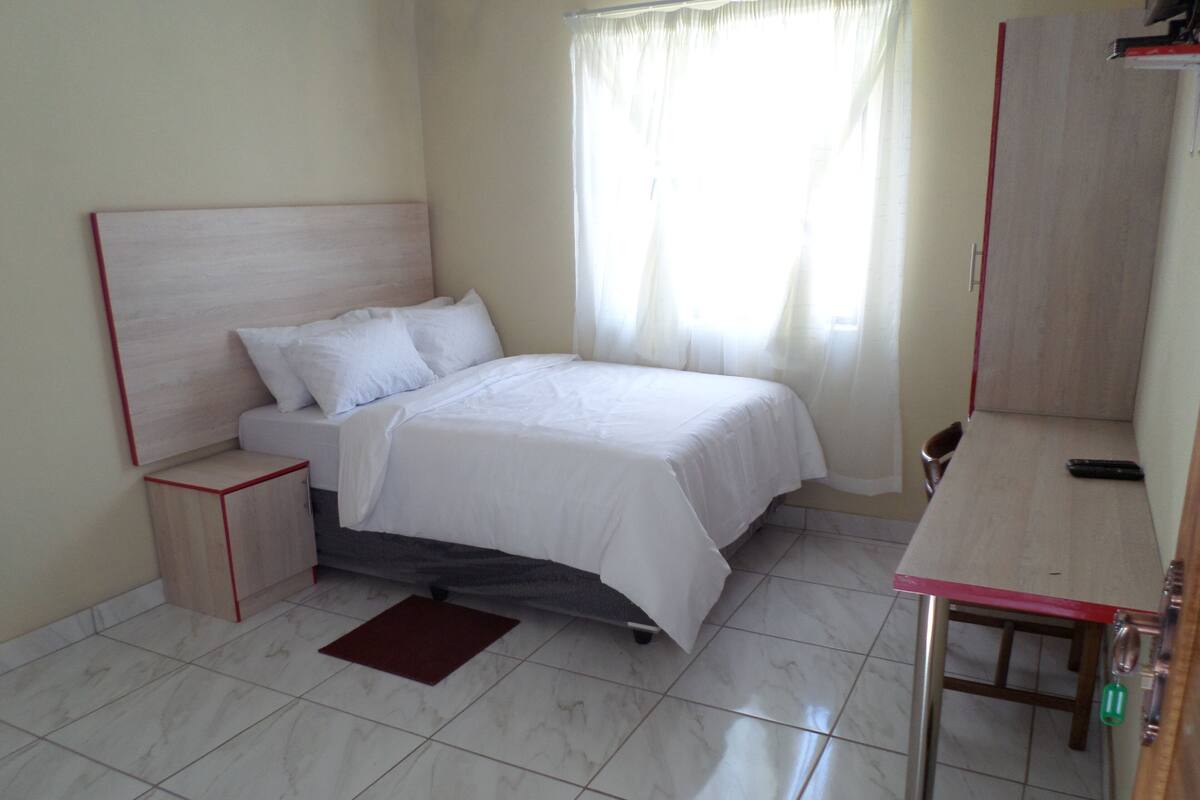 A bedroom with a bed, bedside table, and a desk with a chair.
