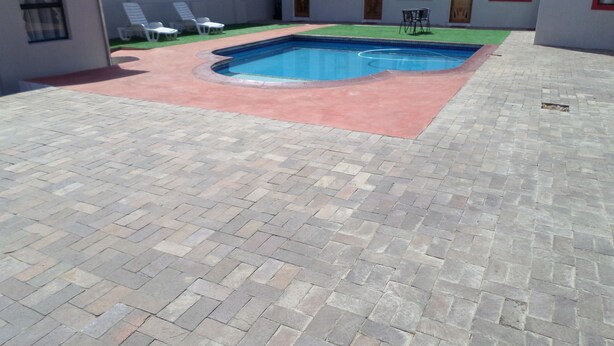 Une piscine bordée de rouge, entourée d’une terrasse dallée.