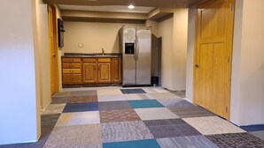A hallway with a kitchen area, featuring wooden cabinets, a stainless steel refrigerator, and a patterned carpet. - 5 Bedrooms and a Great Location (Sioux Falls)