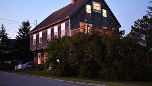 A two-story house with a dark wooden exterior, a visible front porch, and a car parked in the driveway.