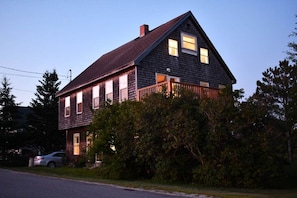 A two-story house with a dark wooden exterior, a visible front porch, and a car parked in the driveway.