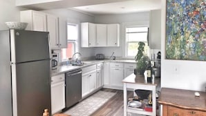 A modern kitchen with white cabinets, a black refrigerator, and a wooden chair.